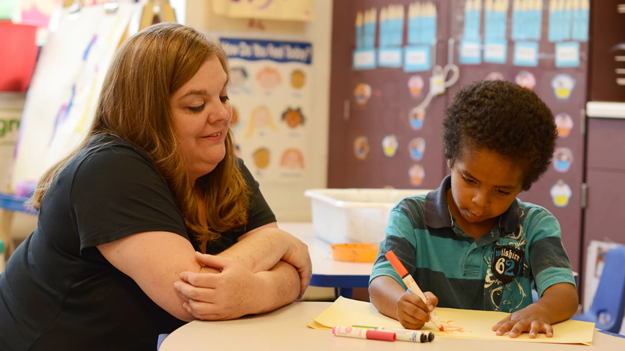 Teacher watches a student coloring in a classroom